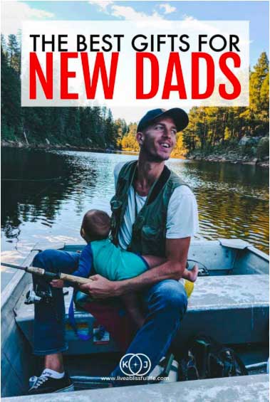 A smiling man on a boat holding a fishing pole while carrying a baby