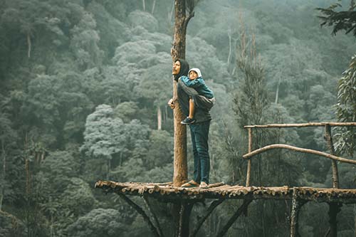 man holding onto a tree trunk with a young boy on his back